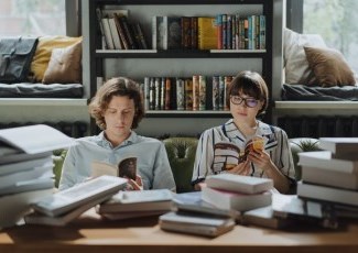 Photo of a couple sitting on a couch reading books with a shelves of books behind them. Photo by cottonbro from Pexels. 